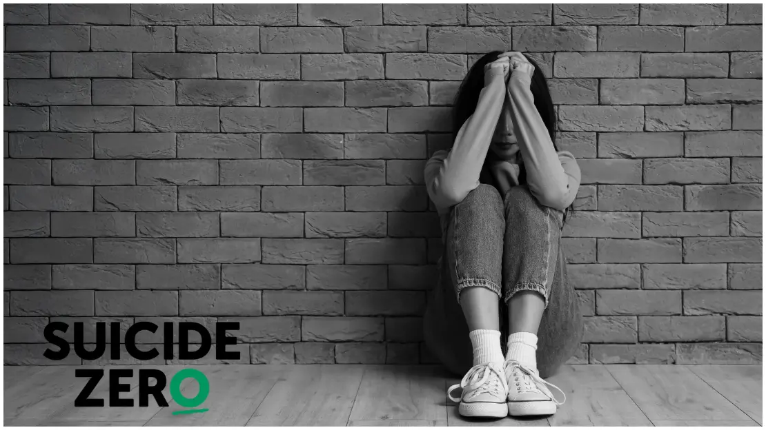 Person sitter på golvet med armarna framför ansiktet. I hörnet finns loggan för Suicide Zero.