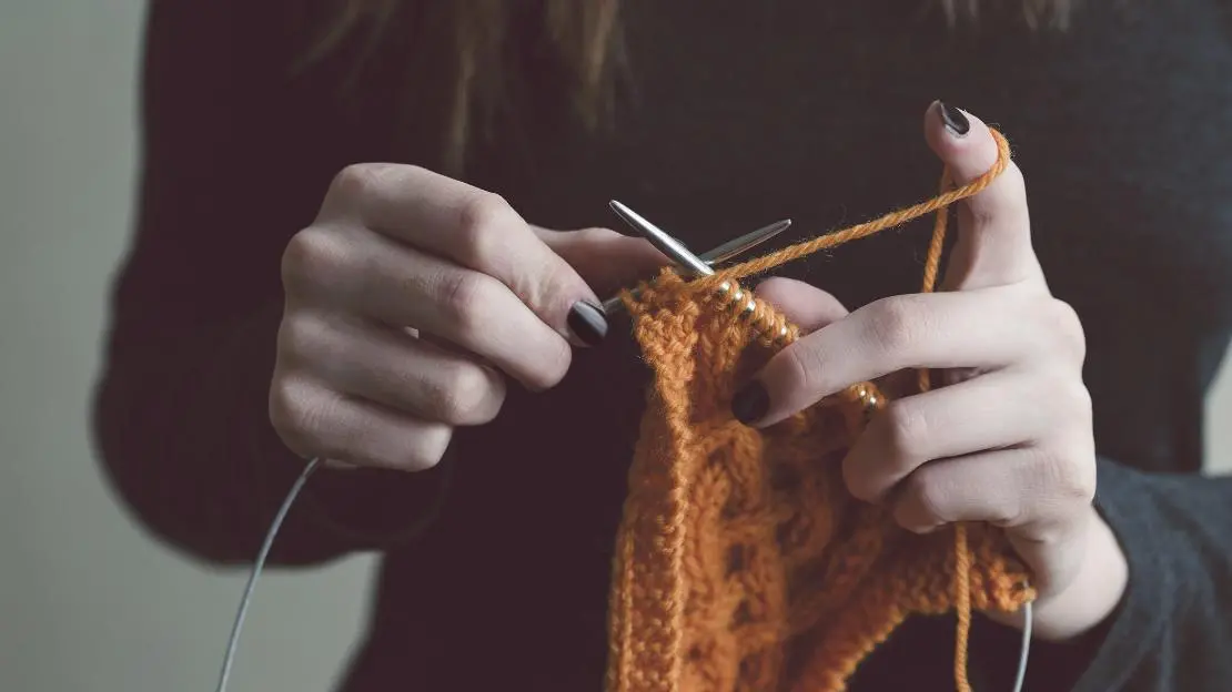 Person stickar med orange garn.  