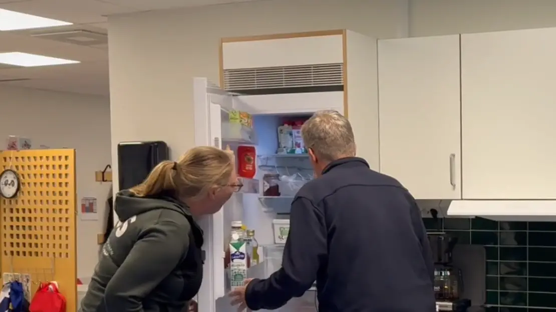 Två personer står och tittar in i ett kylskåp fullt med mat.