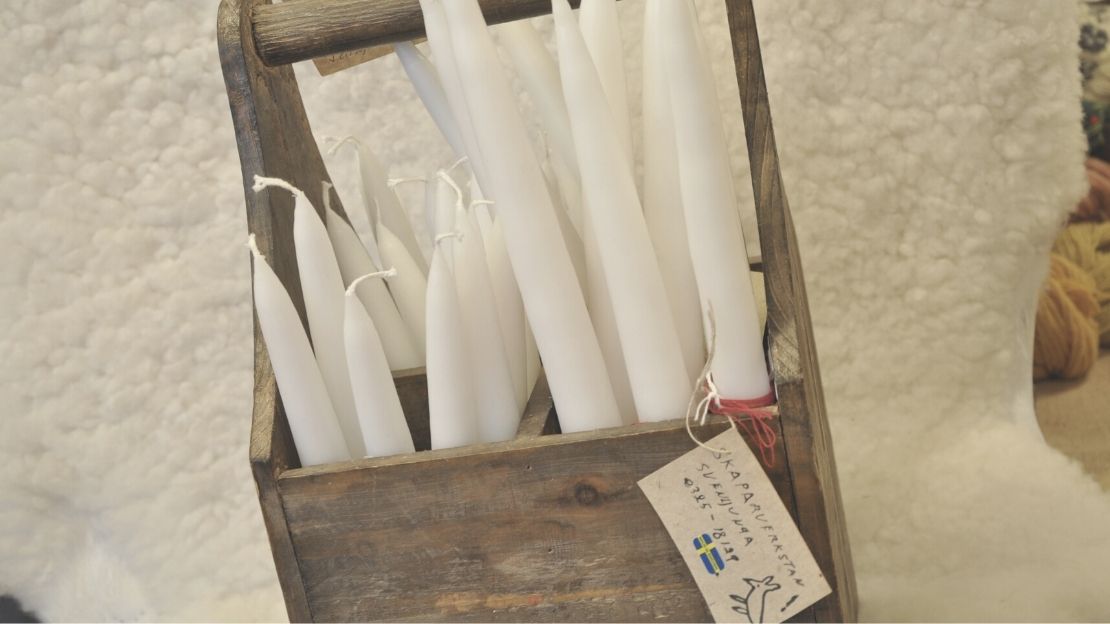 gammal träback fylld med vita handstöpta ljus i två olika längder, framför hänger en lapp med texten "Skaparverkstan Svenljunga"