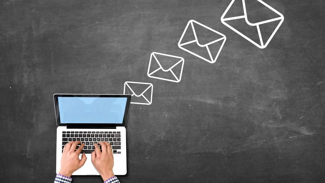 Händer skriver på tangentbordet på en laptop, ovanför den svävar symboler för kuvert.