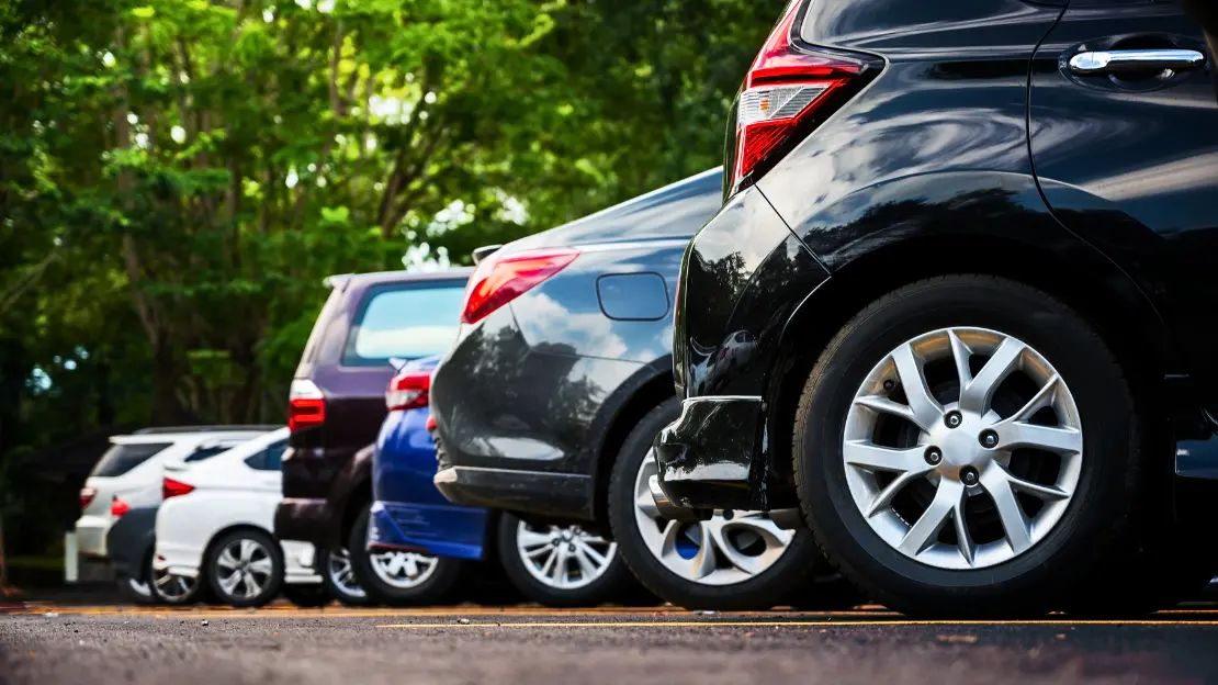 Bilar som står på parkering taget från sidan med gröna buskar i bakgrunden.