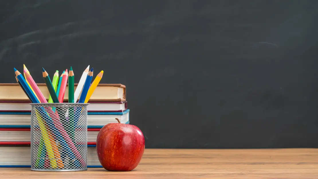 Skrivbord med ett rött äpple, pennor och block.