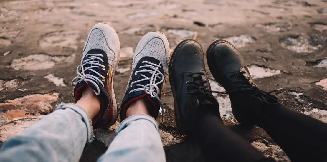 två personers fötter, den ena har kängor den andra gympaskor.