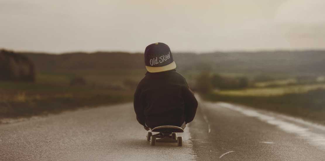 en liten kille som sitter på en skateboard som rullar ner för en väg 