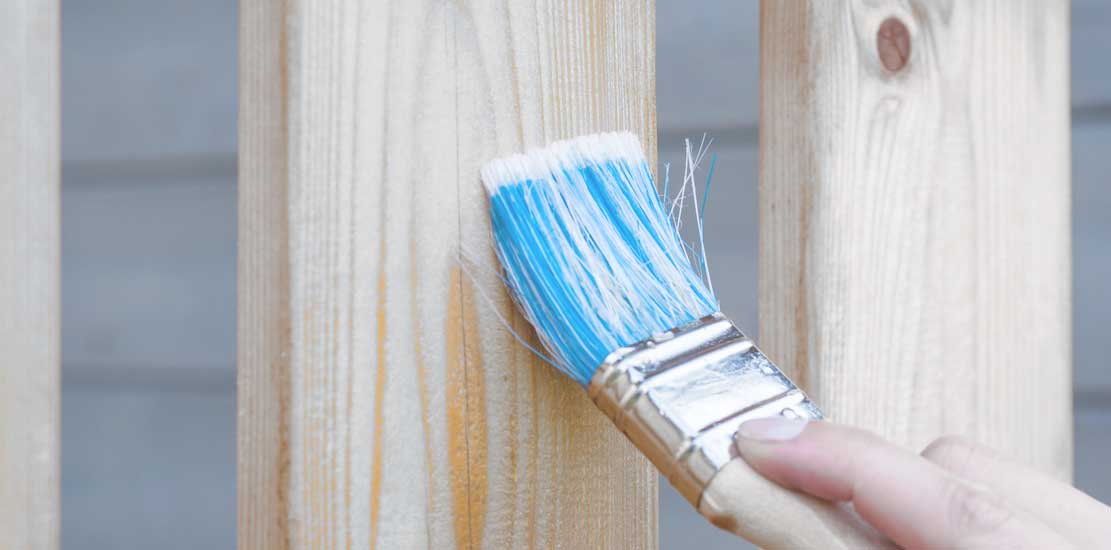 en person målar på trä, man ser målarpenseln och en del av handen