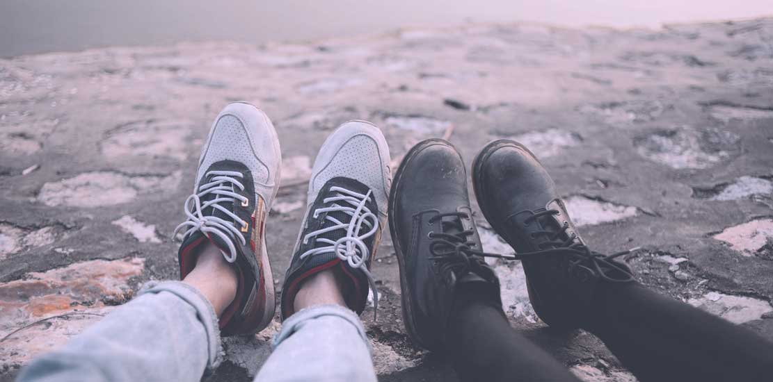 Två personers fötter bredvid varandra, ena med sneakers och den andra med kängor.