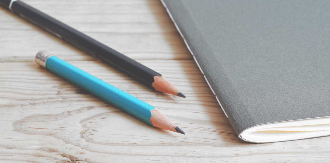 två korta pennor som ligger bredvid en tunn bok 