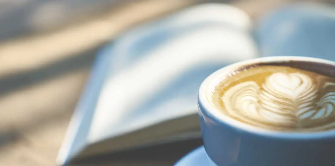 någon som sitter och dricker kaffe med en bok framför sig