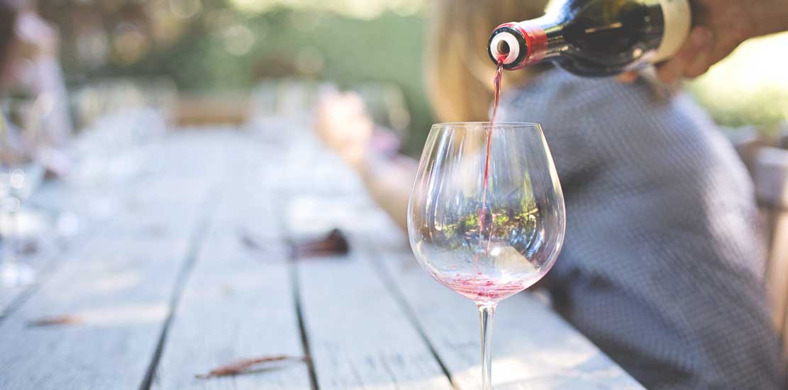person häller upp ett glas rött vin på ett trädäck