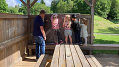 En vuxen och fyra barn tittar ut genom en trävägg.