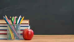 Skrivbord med ett rött äpple, pennor och block.