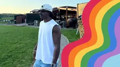 Mörkhyad man i ljusa kläder står utomhus med en teckning på en regnbåge bredvid.