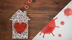 ett litet vitt hus skapat av garn på ett träbord. på huset är det ett rött hjärta även det i garn, istället för rök från skorstenen kommer det små röda hjärtan, även dom i garn.